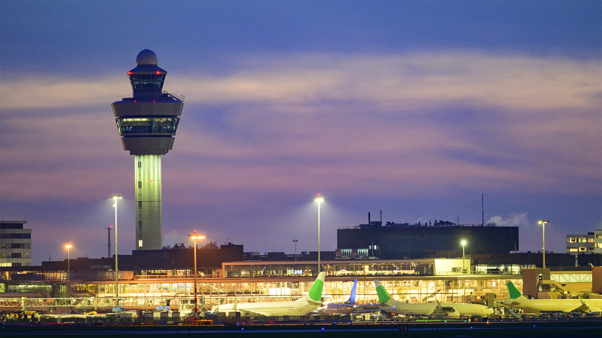 Schiphol airport with various airplanes at night. Schiphol is one of the busiest and largest airports in Europe, located near Amsterdam, Netherlands. It serves as a major hub for international flights and is a key gateway to Europe.
