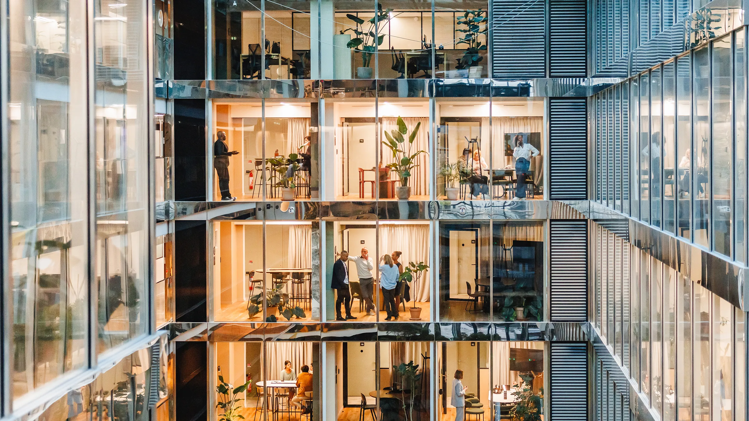 Men and women of various backgrounds collaborate and work independently in a spacious, well-lit office setting, each attired suitably for a professional setting, using modern tools and technology.